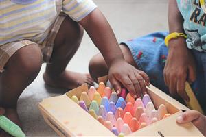 children reaching into box of sidewalk chalk