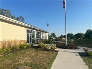 Exterior view of the Kingswood Actvity Center brick and concrete building with flowers, a sidewalk, and flagpole to the right. Playground is in the background.