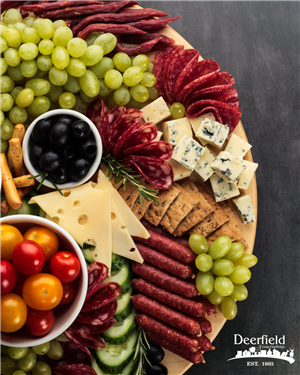 Photo of a wooden cutting board with a variety of meats, cheese, crackers, and fruit on a gray background with Deerfield Township logo