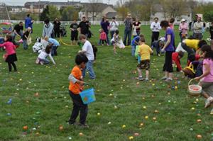 Color easter eggs scattered on the grass while a group of children do an Easter Egg hunt