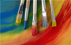 Five paintbrushes laid on paper painted in rainbow colors.