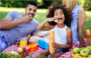 Family smiling and eating a picnic lunch in the park.