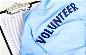 T-shirt with the word Volunteer on the back laying on top of a clipboard with a sign-in sheet on it.