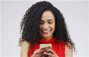 A woman smiling and looking at her phone.