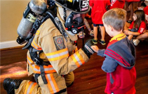 A firefighter in full gear with oxygen pack kneeling and giving a fist pump to a young child.