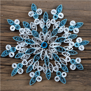 A blue and white snowflake made out of rolled strips of paper on a wooden background